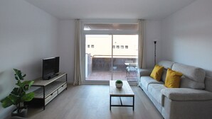 Una sala de estar moderna con un sofá, una mesa de centro, un televisor sobre un mueble bajo y una planta.
