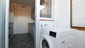 A compact laundry room with a washing machine, a small window, and a door leading to a kitchen area.