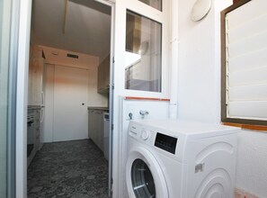 A compact laundry room with a washing machine, a small window, and a door leading to a kitchen area.
