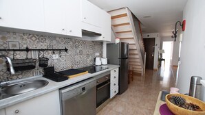 Una cocina con armarios blancos, un lavamanos de acero inoxidable, lavavajillas, refrigerador y tabla de madera con un tazón de piñones.