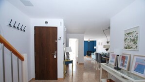 Un pasillo con una puerta de madera, una consola blanca con cestas y una pared azul decorada con marcos.