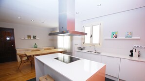 Una cocina moderna con armarios blancos, una isla central con placa de inducción, una campana extractora de acero inoxidable y un ventanal sobre el fregadero.