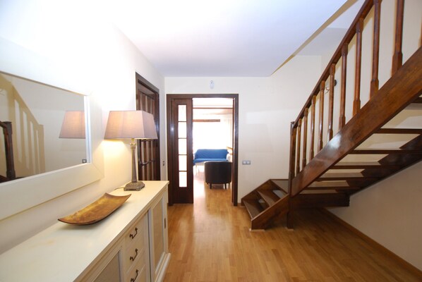 A hallway with a wooden staircase, a lamp, and a mirror on the wall.