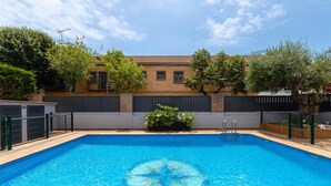 A rectangular swimming pool with a clear blue center, surrounded by a grey fence, and a building with a brown facade and windows in the background. - Gregal - Aparthotel with Swimming Pool (Vilassar de Mar)
