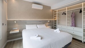 A modern hotel room with a large bed, built-in wardrobe, bedside tables, and an air conditioning unit.
