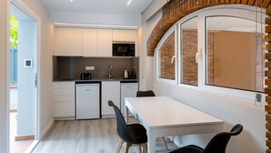 A compact kitchen with white cabinetry, a microwave, and a dishwasher. There is a dining table with chairs and a window with a view of the outside.