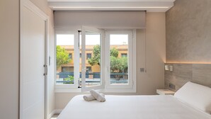A modern hotel room with a large bed, a nightstand, and a window with a view of buildings and trees.