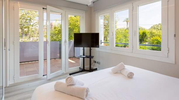 A hotel room with a bed, a TV, and a balcony with a view of greenery. - Ponent - Aparthotel with Swimming Pool (Vilassar de Mar)