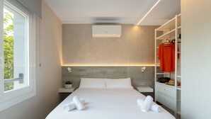 A modern hotel room with a large bed, a wardrobe, a bedside table, and a window with a view of greenery. - Ponent - Aparthotel with Swimming Pool (Vilassar de Mar)