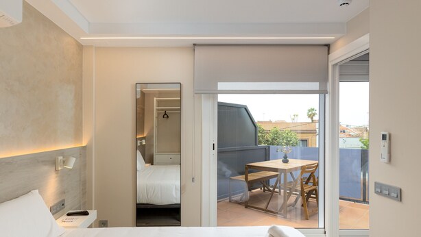 A hotel room with a bed, bedside table, and a view of the balcony with a table and chairs. - Xaloc - Aparthotel with Swimming Pool (Vilassar de Mar)