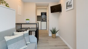 A modern living room with a grey sofa, a small dining table, and a kitchen in the background. - Xaloc - Aparthotel with Swimming Pool (Vilassar de Mar)