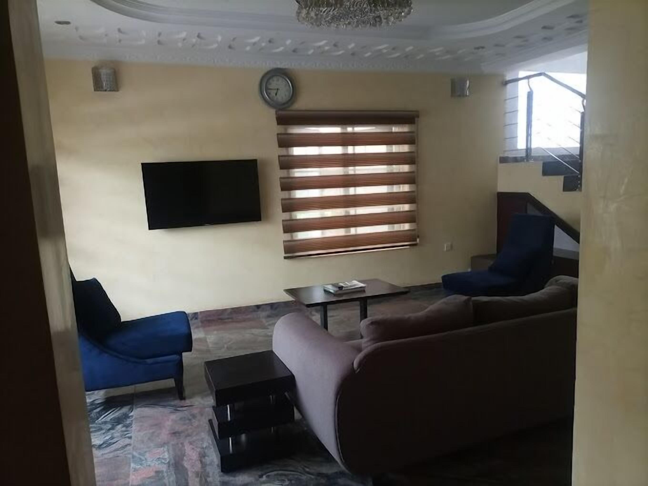 A living room with a sofa, two armchairs, a coffee table, a TV, and a window with blinds.
