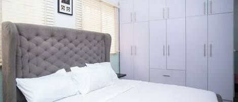 A bedroom with a large bed, white bedding, a tufted headboard, a wardrobe with multiple doors, and a framed picture on the wall.
