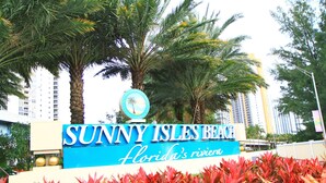 Schild für Sunny Isles Beach, mit Palmen und einem Gebäude im Hintergrund.