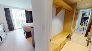 A modern hotel room with a bed, a wooden bench, a mirror, and a door leading to a balcony.
