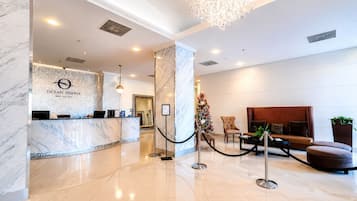 A hotel reception area with a marble counter, a Christmas tree, and a seating area with a sofa and armchairs.