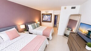 Una habitación de hotel con dos camas, un televisor, un aparador y un cuadro en la pared.