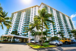 A multi-story hotel with a white facade, numerous balconies, and palm trees in the foreground.