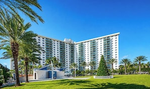 A multi-story hotel with a modern design, featuring a large central atrium and a well-maintained lawn with palm trees. - O. Reserve 1017  FlatsAway  1 Bedroom Ocean View (Sunny Isles)
