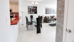 Un espacio habitable moderno con comedor, un conjunto de sofás y una cocina visible a través de un umbral abierto.