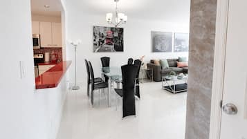 A modern living space with a dining area, a sofa set, and a kitchen visible through an open door.
