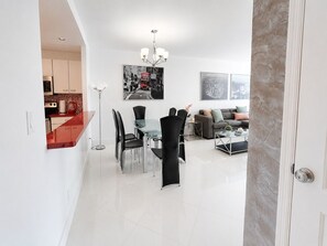 A modern living space with a dining area, a sofa set, and a kitchen visible through an open door.