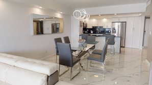 A modern kitchen with white cabinets, a central island, and a dining area with a glass table and chairs. - OR1019 - Modern Ocean View Apt  Steps to the Beach (Sunny Isles)