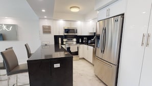 A modern kitchen with a central island, stainless steel appliances, and white cabinetry. - OR1019 - Modern Ocean View Apt  Steps to the Beach (Sunny Isles)