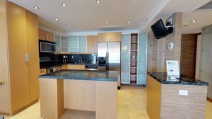Una cocina moderna con armarios de madera, una isla central, electrodomésticos de acero inoxidable y un televisor de pantalla plana montado en la pared.