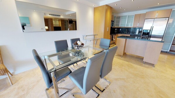 A modern kitchen with stainless steel appliances, a dining area with a glass table and chairs, and a large mirror above the dining table.