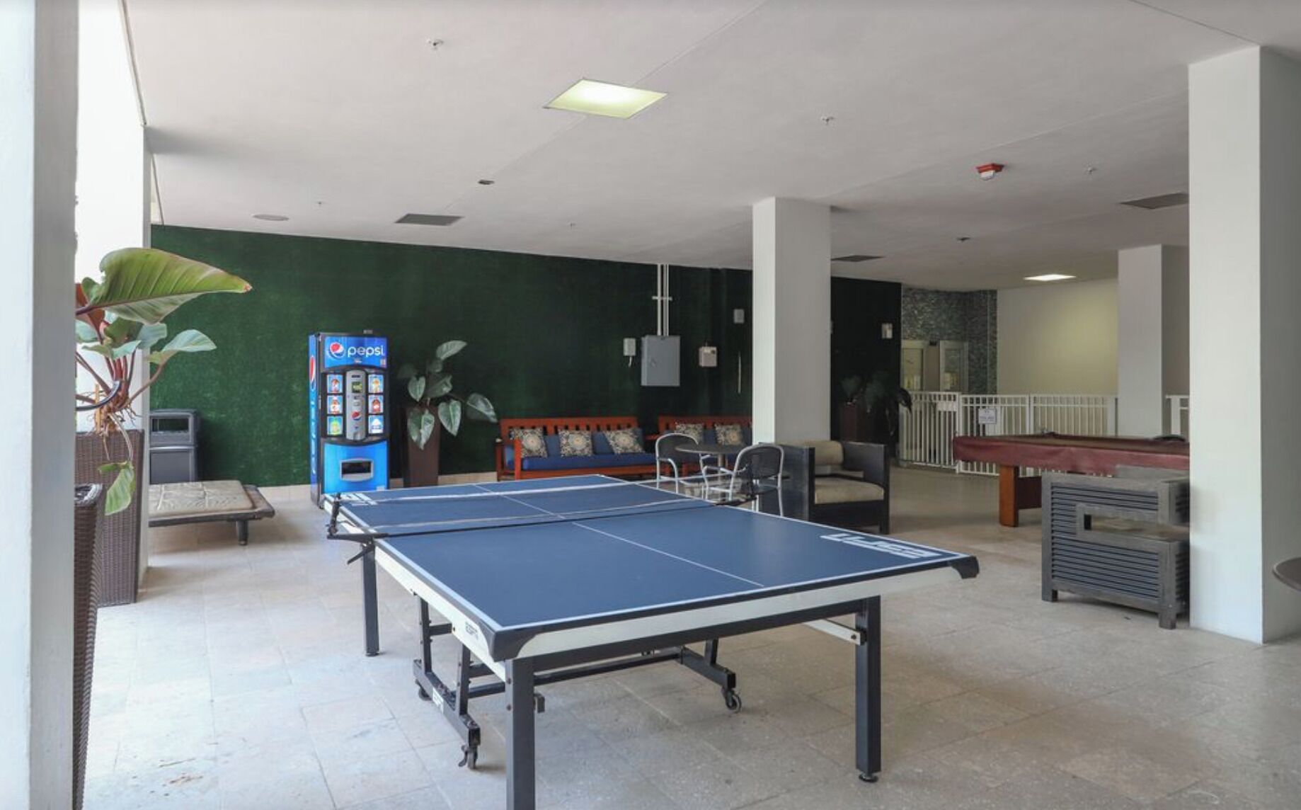 Une table de ping-pong dans un espace intérieur spacieux, avec un mur vert, des sièges et une table de billard.