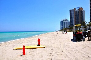 Una spiaggia con torri di salvataggio, una sedia per i bagnini, un surfboard giallo e un carrello da golf.
