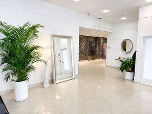A clean, modern lobby with a large potted plant, a glass door leading to an elevator, and a mirror on the wall. - Large 1 Bedroom Bay View | Ocean Reserve OR610 (Sunny Isles)