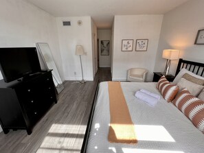 Et hotelværelse med seng, fjernsyn, kommode, stol og lampe.
