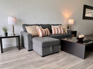 A modern living room with a grey sectional sofa, two side tables with lamps, and a glass coffee table.
