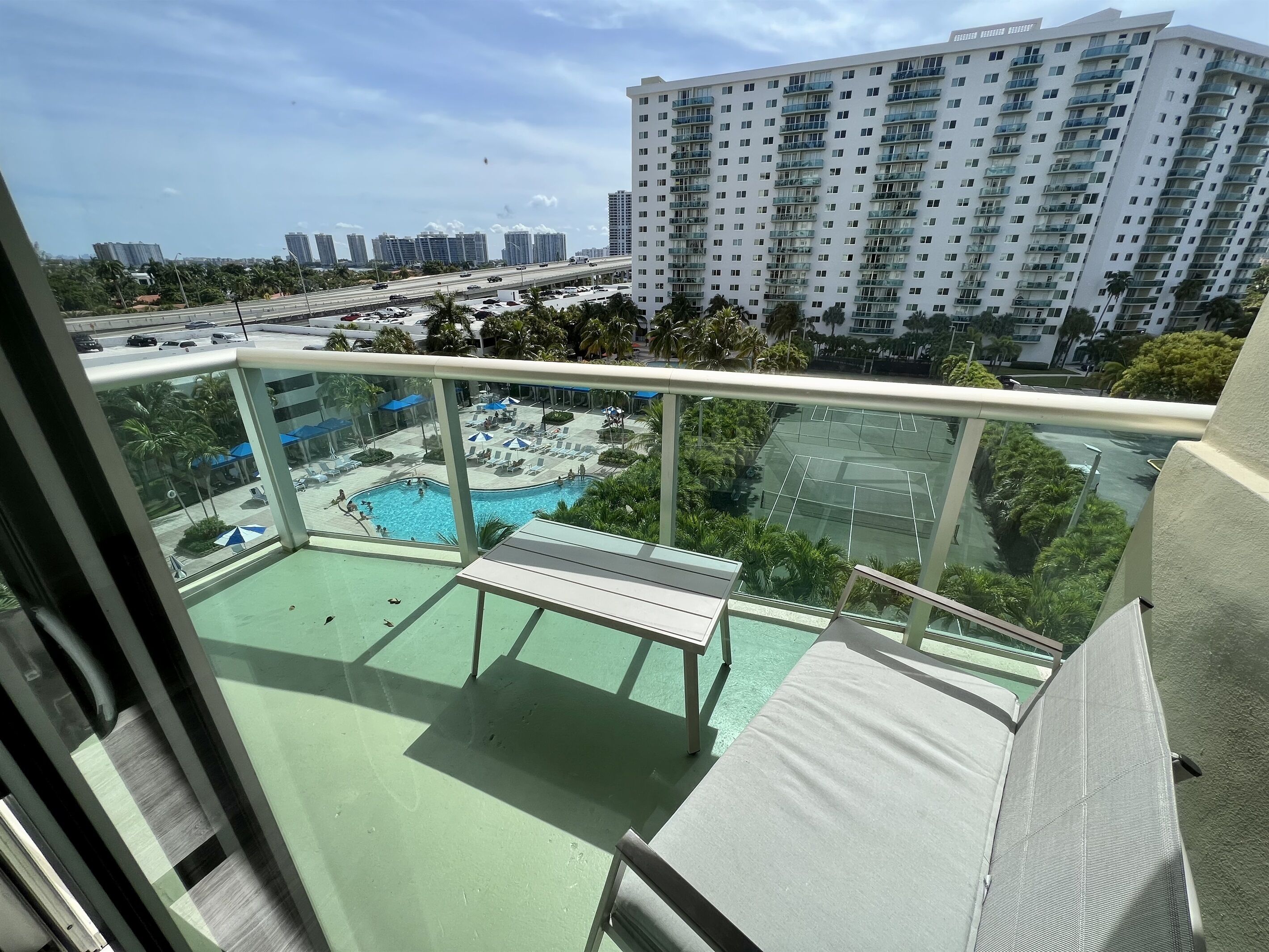 Un balcon donnant sur une piscine et un court de tennis, le tout entouré d’immeubles de grande hauteur.