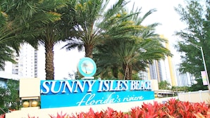 Señal de Sunny Isles Beach con palmeras y un edificio al fondo.