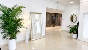 A clean, modern lobby with a large potted plant, a glass door leading to an elevator, and a mirror on the wall.