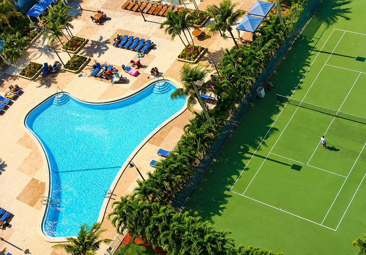 Une piscine entourée de chaises longues et un court de tennis.