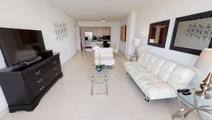Una sala de estar moderna con televisor, cómoda negra, sofá blanco y mesa de centro de vidrio.