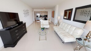 Una sala de estar moderna con televisor, cómoda negra, sofá blanco y mesa de centro de vidrio.