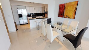 Una cocina moderna con armarios blancos, electrodomésticos de acero inoxidable y una mesa de comedor de vidrio con sillas blancas y negras.