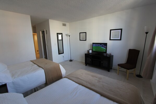 A hotel room with two beds, a television, a desk, and a chair.