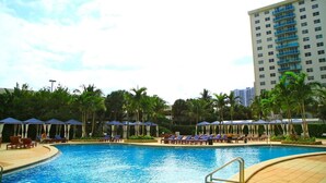 A swimming pool with lounge chairs and umbrellas, surrounded by palm trees and a tall building in the background. - Ocean View Apartment  w/Parking in MIAMI-OR-805 (Sunny Isles)
