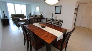 A dining area with a wooden table, chairs, and a chandelier. There is a sofa and a coffee table in the background. - Ocean View Apartment  w/Parking in MIAMI-OR-805 (Sunny Isles)
