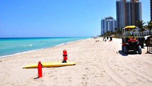 A beach with lifeguard stands and a lifeguard chair, a yellow surfboard, and a golf cart. - Ocean View Apartment  w/Parking in MIAMI-OR-805 (Sunny Isles)