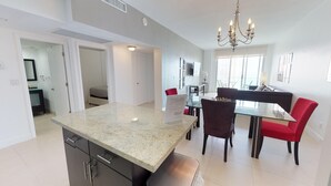 A modern kitchen with granite countertops, a dining area with red chairs, and a chandelier. - PH11 Luxury Ocean View Apartment (Sunny Isles)