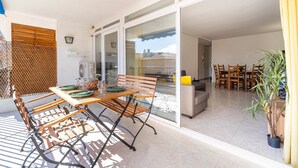 A spacious patio with a wooden table and chairs, a sliding glass door leading to an indoor dining area, and a potted plant. - Cosy apartment near the beach in a quiet area · 240 UHC EL CRANC (Salou)