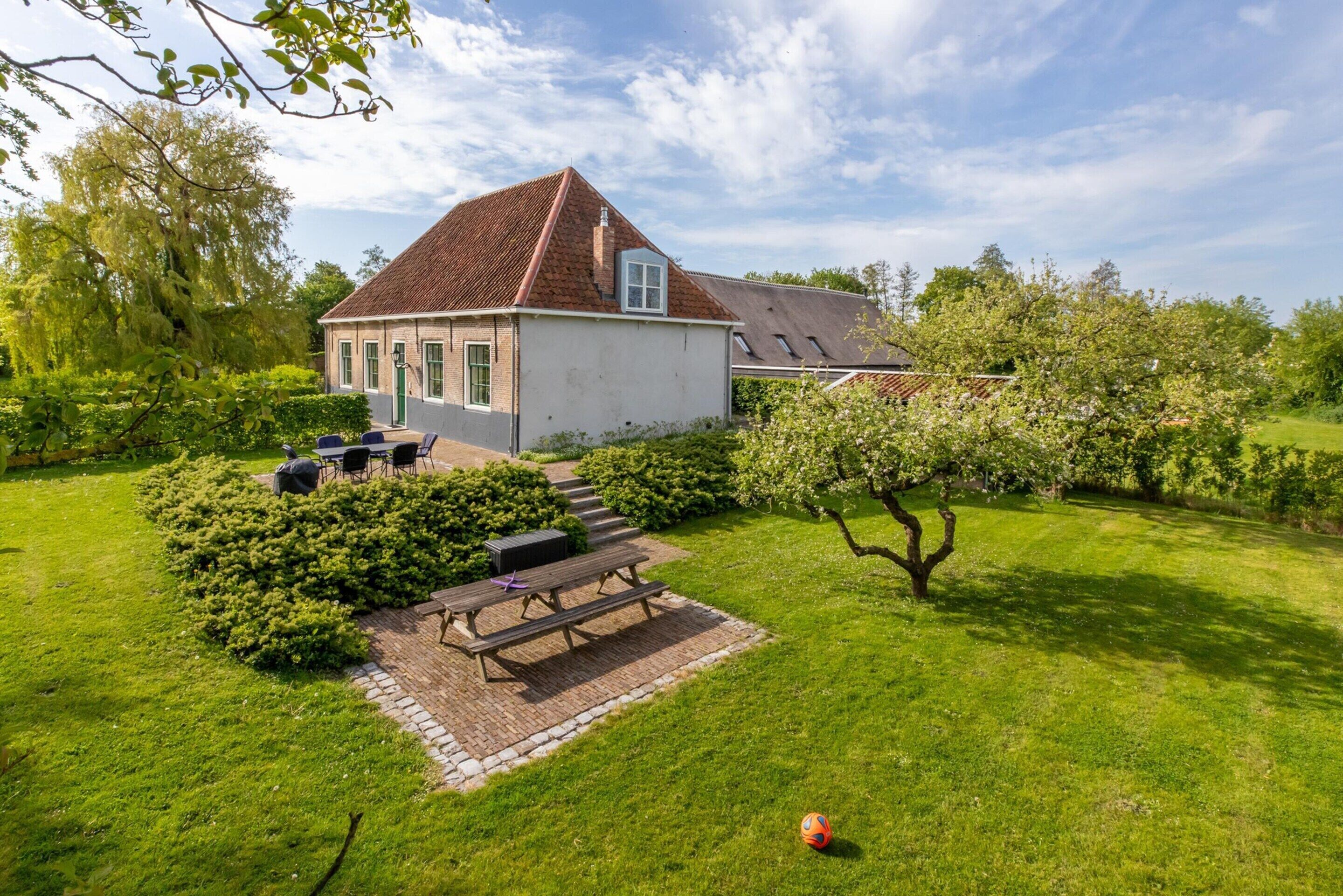 A house with a sloped roof, a paved patio with a table and chairs, and a well-maintained lawn.