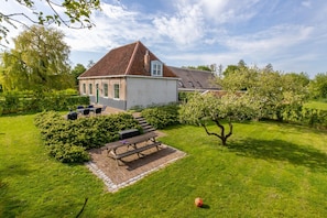 A house with a sloped roof, a paved patio with a table and chairs, and a well-maintained lawn. - Farmhouse in Zeeland With Windmill Views (Heinkenszand)
